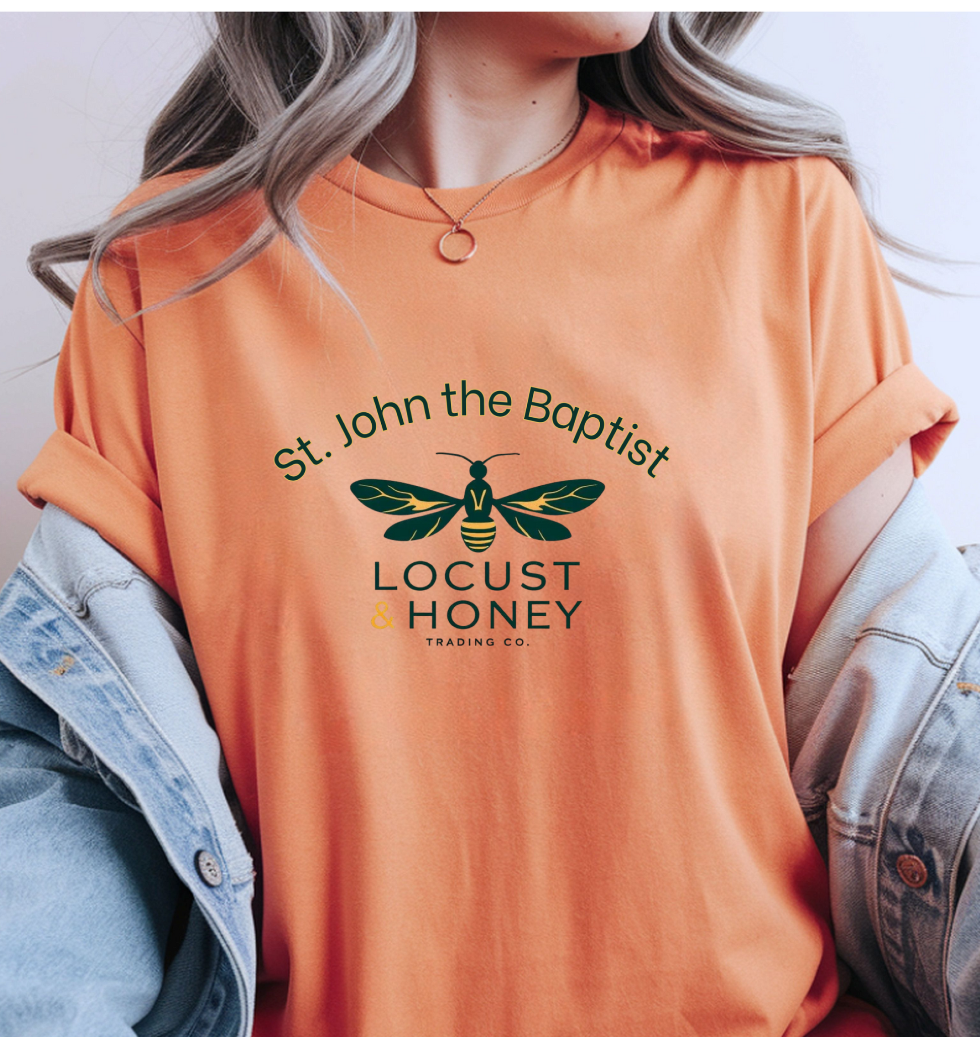 A female wearing an orange shirt with a locust graphic design that says 'St. John the Baptist Locust & Honey Trading Co."