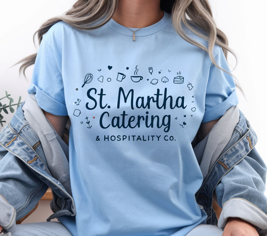 A female wearing a light blue shirt that says " St. Martha Catering & Hospitality Co"