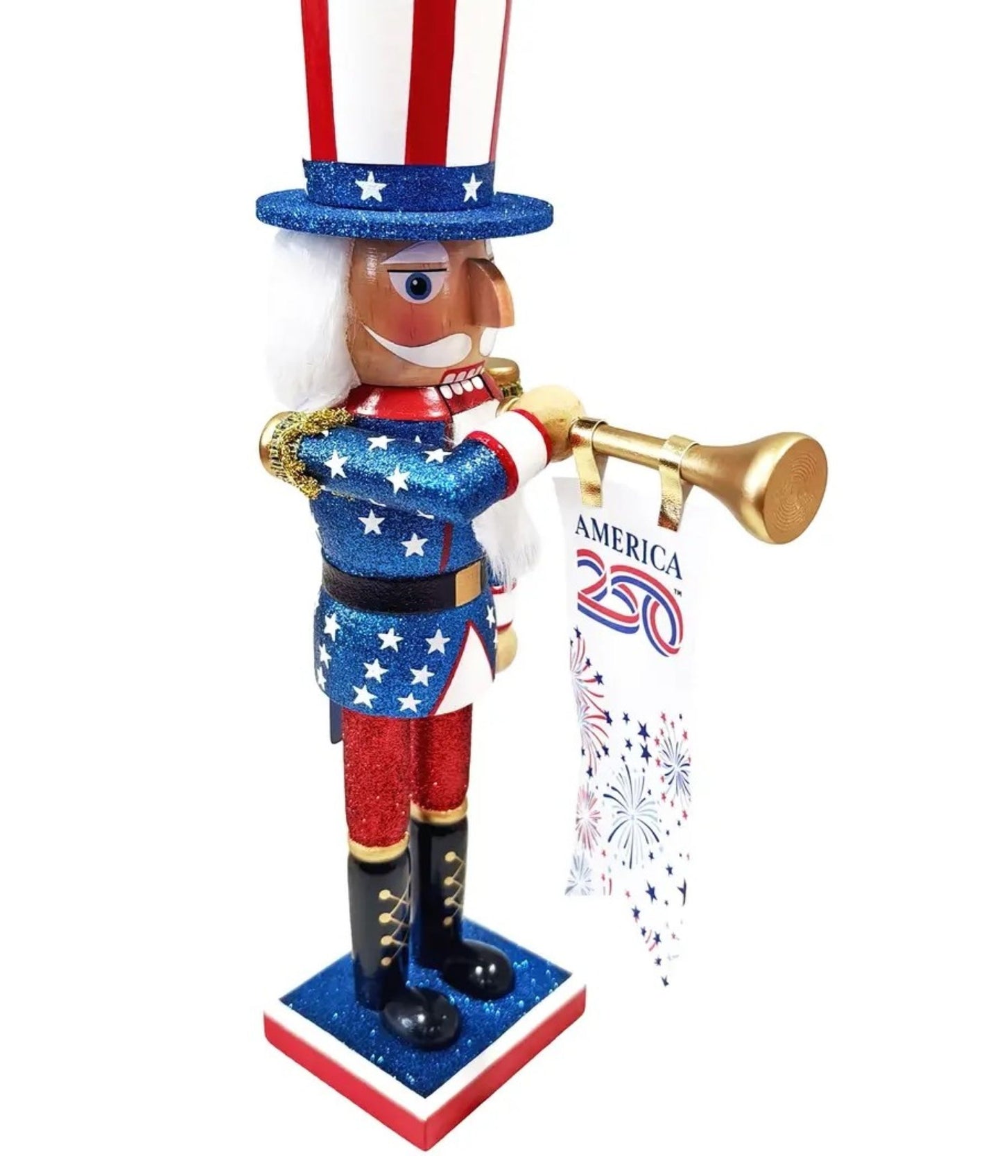 A patriotic Uncle Sam nutcracker figurine holding a gold trumpet and a banner that reads 'AMERICA 250' with fireworks graphics. The figurine features a red, white, and blue glittery design with white hair and a red, white, and blue striped hat, set against a plain white background.