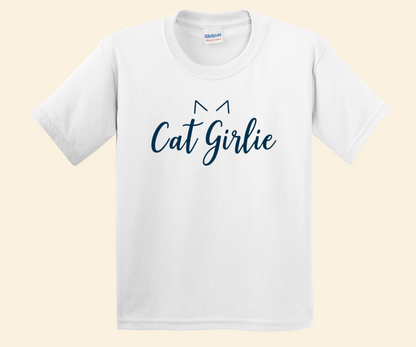 A white short-sleeve crewneck t-shirt featuring the text 'Cat Girlie' in dark blue script, with a simple cat ear graphic above the letters, displayed on a light beige background.