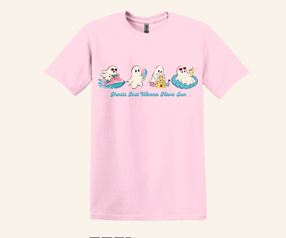 A light pink short-sleeve crewneck t-shirt featuring a cartoon graphic of four ghosts relaxing on pool floats with the text 'Ghosts Don't Wanna Have Sun' printed in blue script below them.