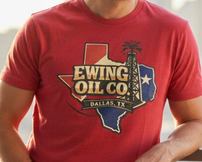 A red short-sleeve crewneck t-shirt featuring a graphic of the state of Texas filled with a red, white, and blue design, overlaid with the text 'EWING OIL CO. DALLAS, TX' and an oil derrick illustration.