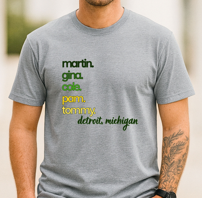 A man wearing a heather gray t-shirt with a colorful text graphic listing names and 'detroit, michigan' on the chest.