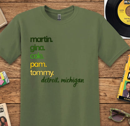 An olive green short-sleeve t-shirt with a personalized list of names and locations printed on the front, laid flat on a rustic wooden background with vintage record and book props.