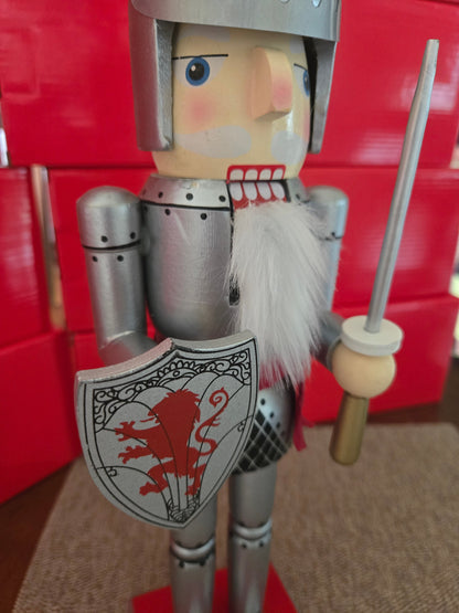 All I Need Designs 14" wooden knight nutcracker in silver armor with red shield and sword, featuring a white beard and red plume.