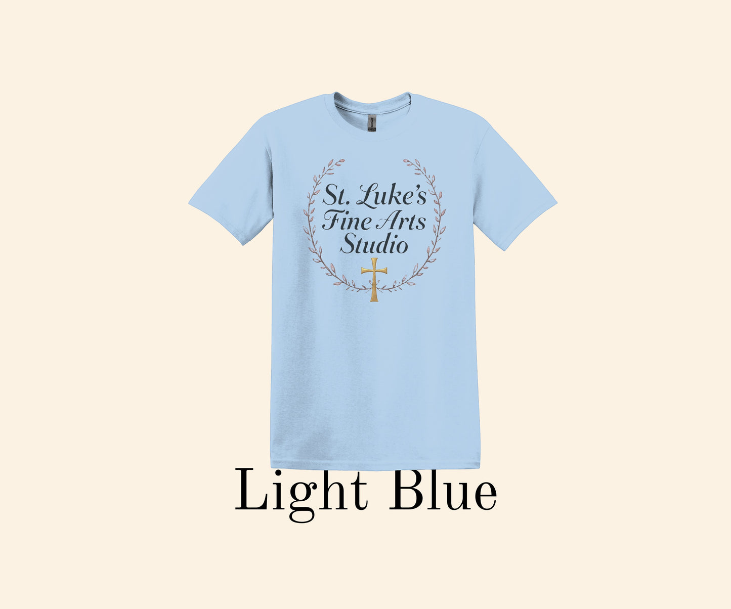 All I Need Designs light blue cotton blend t-shirt with "St. Luke’s Fine Arts Studio" and gold cross within a laurel wreath.