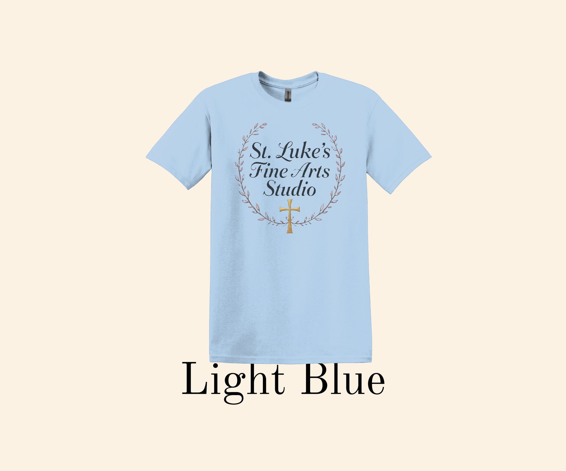 All I Need Designs light blue cotton blend t-shirt with "St. Luke’s Fine Arts Studio" and gold cross within a laurel wreath.