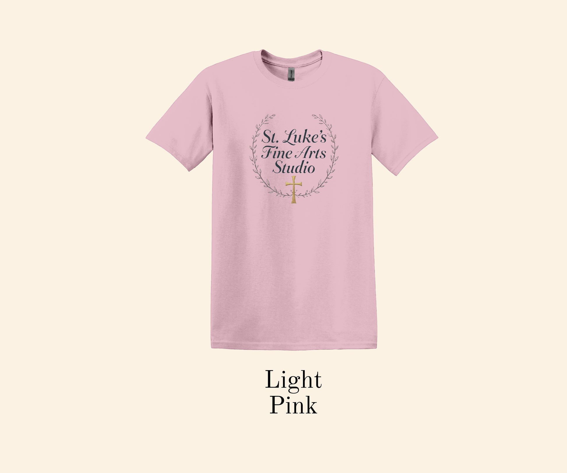 All I Need Designs light pink cotton blend t-shirt with St. Luke’s Fine Arts Studio text and gold cross within a laurel wreath.