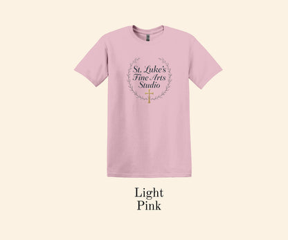 All I Need Designs light pink cotton blend t-shirt with St. Luke’s Fine Arts Studio text and gold cross within a laurel wreath.