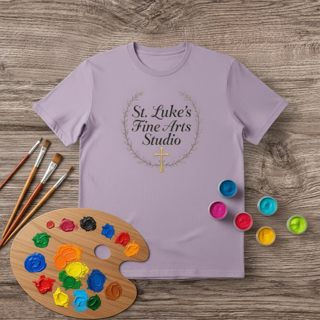 All I Need Designs light purple cotton blend t-shirt with "St. Luke’s Fine Arts Studio" and a gold cross within a laurel wreath.